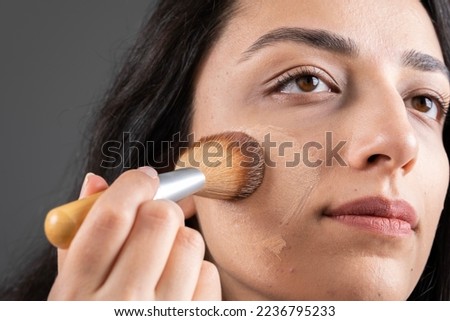 Tonal foundation, close up image of attractive woman applying liquid tonal foundation. Holding and using brush making her own make up. Isolated gray background with copy space. Skin care concept idea.