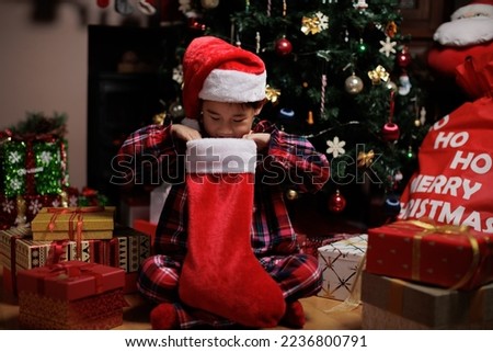 young girl wearing Santa hat was searching Christmas stocking in front of Christmas tree