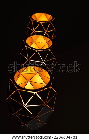 Black lamps with a geometric pattern, three lamps on a black background, burning with warm light, with a graphic pattern