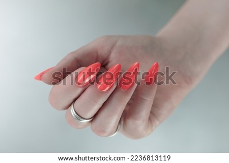 Woman hand with long nails and light orange neon manicure holds a bottle of nail polish	