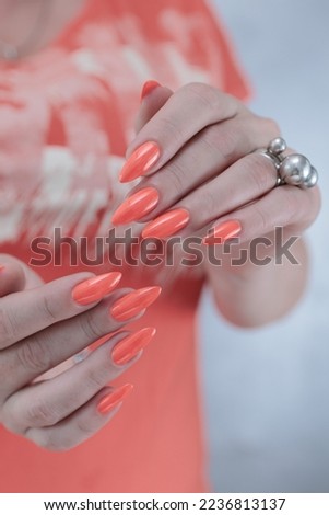 Woman hand with long nails and orange neon manicure holds a bottle of nail polish