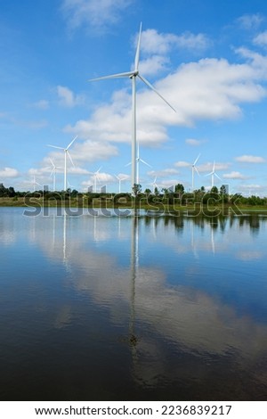 Powerful Wind turbine farm for pure energy production on Beautiful clear blue sky with white clouds and wind turbine farm reflection on lake. renewable energy Royalty-Free Stock Photo #2236839217