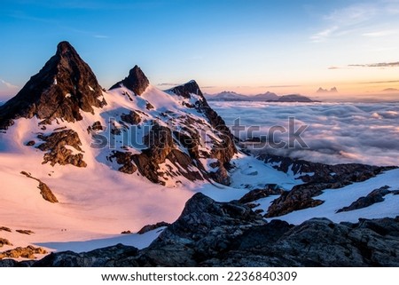 Sunrise Illuminates an Ocean of Clouds and Snowfield Peak as Two Small Climbers Ascend the Glacier Below. North Cascades National Park, Washington Royalty-Free Stock Photo #2236840309
