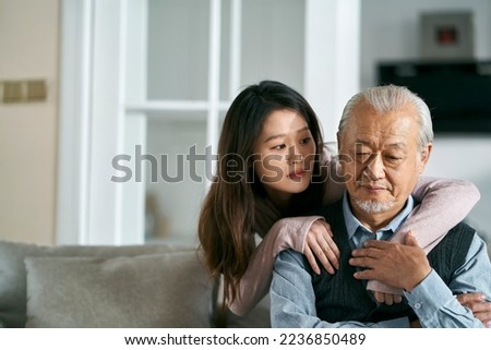 sad senior asian father sitting on couch in living room at home consoled by adult daughter Royalty-Free Stock Photo #2236850489