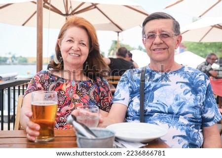 Senior hispanic couple drinking something cool, beer and water, at an outdoor table in a restaurant on a summer evening.