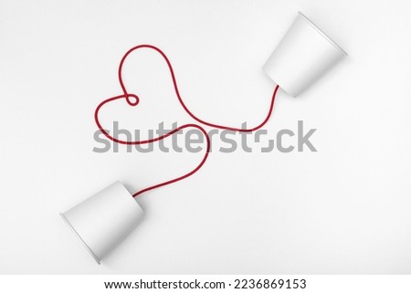 white cups phone and red string with heart shape