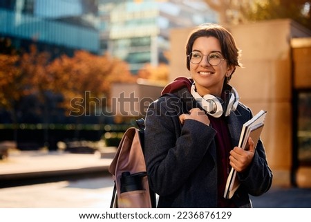 Young happy woman carrying backpack and books while going on a lecture at campus.  Royalty-Free Stock Photo #2236876129