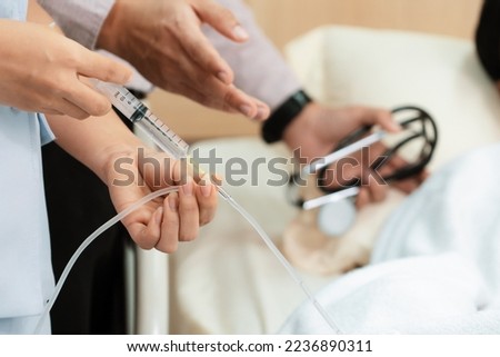 Doctor and nurse inject medicine, dosage into IV tube providing medical treatment to patient in sterile room at hospital. Fragile patient receive medical care on sick bed in recovery room.
