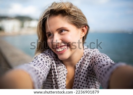 Portrait of attractive young woman smiling and taking selfie against the sea