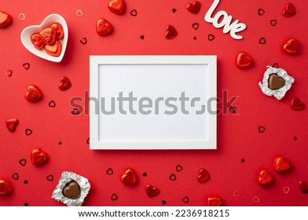 Valentine's Day concept. Top view photo of white photo frame heart shaped chocolate candies saucer inscription love and confetti on isolated red background with blank space