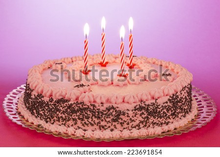 Strawberry and chocolate cake with lighted birthday candles on a pink background.