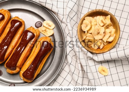 Plate of tasty chocolate eclairs and banana on fabric background, closeup