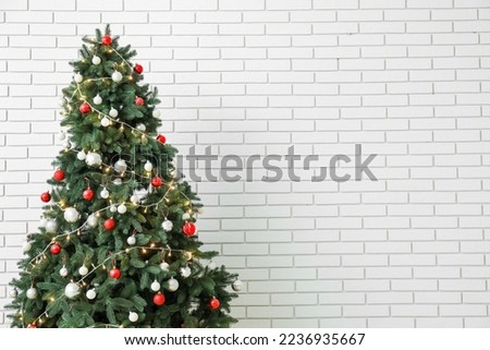 Glowing Christmas tree near white brick wall