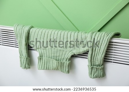 Warm sweater drying on electric radiator near green wall, closeup