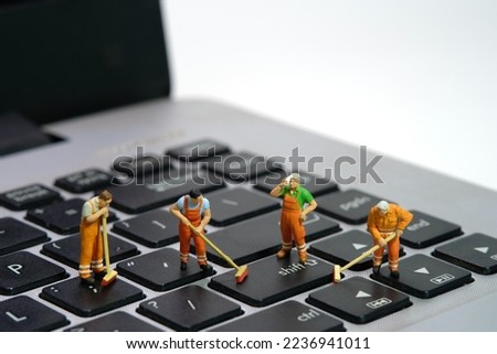 Miniature people toy figure photography. Group of sweeper workers cleaning notebook laptop keyboard using broom, brush. Isolated on white background. Image photo