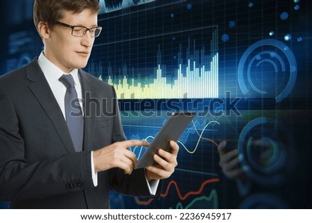 Attractive young european businessman in glasses using cellphone with digital business graph hologram on blurry blue background. Trade, finance and analysis concept