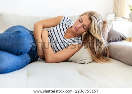 Stomach pain, sick and woman with endometriosis on the living room sofa in home, sleeping with health problem and sad about medical emergency on couch. Hungry person with tummy cramp in the lounge.
