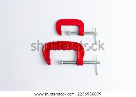 Two red metal clamps of different sizes on a white background. Tools for repair work and DIY projects. Construction, craft, work with wood products. Royalty-Free Stock Photo #2236956099