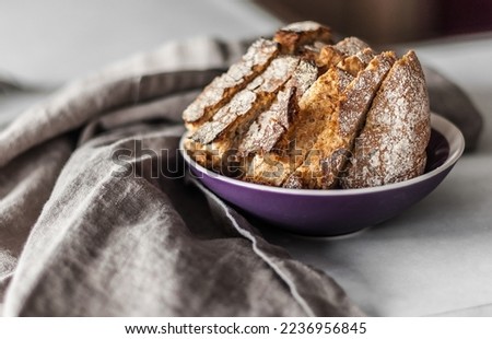 Slices of freshly baked bread in a magenta ceramic plate on a linen apron on the work surface of an island in the kitchen.