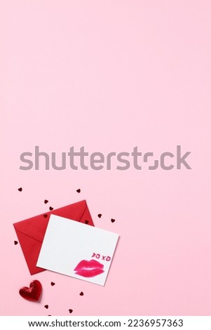 Romantic love letter concept. Blank paper card with lipstick kiss and red envelope on pastel pink background. Happy Valentines Day greeting card mockup.