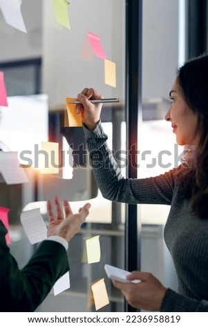 Two young creative team using post it notes in glass wall to writing strategy and business plan.