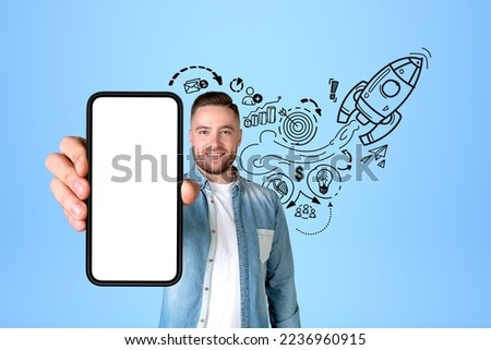 Smiling man portrait showing phone with mockup blank display. Black doodle sketch with start up plan on blue background, graphs and rocket launch. Concept of mobile app Royalty-Free Stock Photo #2236960915