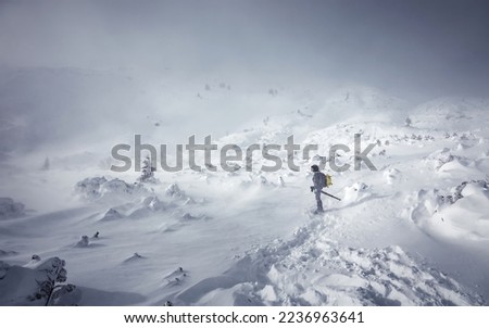 Stunning winter nature landscape. Alone man in snow covered mountain. Hiker, photographer on the snowcapped highland. Outdoors active lifestyle concept. Snowy mountain scenery with cloudy day
