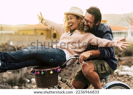 Happy couple enjoy outdoor leisure activity together carrying and using a bike and laughing a lot. Love and friendship with mature man and woman in youthful lifestyle. Concept of joyful and excitement Royalty-Free Stock Photo #2236966833