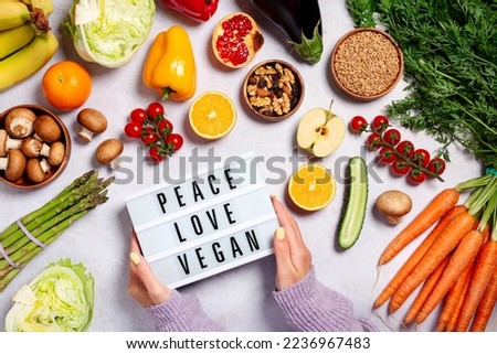 Woman holding lightbox with quote Peace, Love, Vegan on table with raw vegan foods