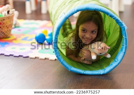 Adorable hispanic girl crawling inside tunnel toy at kindergarten
