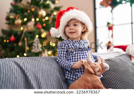 Adorable hispanic girl holding toy standing on sofa by christmas tree at home