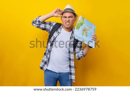 Confused young traveler tourist Asian man wearing casual clothes and hat with a backpack holding city map and put hand on his head isolated on yellow background. Air flight journey concept