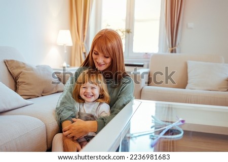 Happy loving family. mother and child girl playing, kissing and hugging. Attractive woman and little girl sitting on comfortable couch at home. Young mother talking communicates with small  daughter.