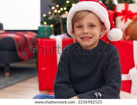 Adorable toddler smiling confident sitting on floor by christmas tree at home