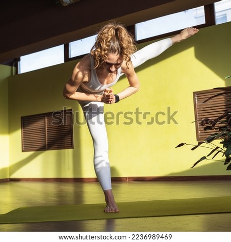 Young Woman, Healthy Lifestyle and Yoga Practitioner, Performs Adhomukha Uthitahasta Padangushthasana Exercise 2, Balance On One Leg, Trains In White Sportswear In Room On Mat