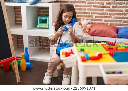 Adorable hispanic girl playing with telephone toy sitting on table at kindergarten