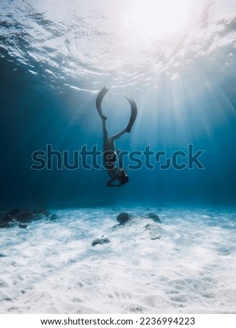 Woman freediver with fins dive to sea bottom. Freediving in blue ocean with sun rays Royalty-Free Stock Photo #2236994223