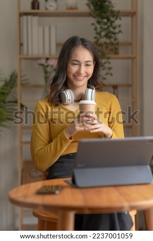 Pretty Asian woman sitting happily working with laptop and drinking coffee smiling and laughing brightly on a comfortable day at home. Royalty-Free Stock Photo #2237001059