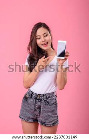 Young cute and happy asian woman excited and using smartphone on pink background.