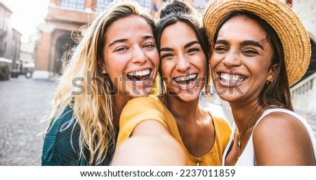 Three multiracial young women taking selfie photo walking on city street - Millenial female friends having fun together outdoors - Friendship, feminist and technology concept