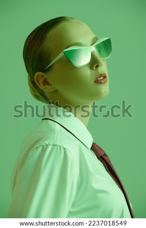 Fashion photo of a gorgeous young woman posing in a white shirt, red tie and stylish elegant sunglasses against a bright green studio background. Successful people. Elegant business style. 