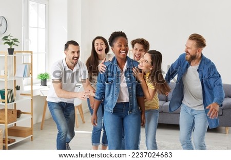 Happy African American woman having fun with several friends at a party at home. Group of cheerful joyful young people hug their friend as they laugh at her joke or congratulate her on great success Royalty-Free Stock Photo #2237024683