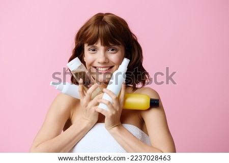  photo of a sweet, joyful woman standing on a pink background with different skin care products, smiling broadly at the camera, pressing them to the cheek