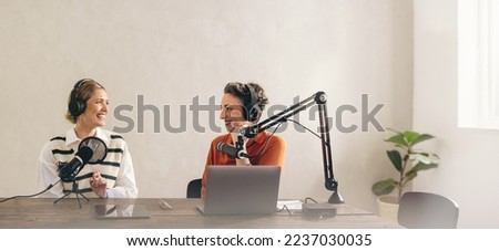 Two happy radio hosts having a great conversation on their show in a home studio. Two cheerful women smiling while recording a live podcast for their social media channel.