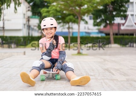 asian child skater or kid girl smile playing skateboard or sitting thumbs up to like on surf skate and fun in skate park for extreme sports to wear helmet elbow wrist knee support for body safety Royalty-Free Stock Photo #2237057615