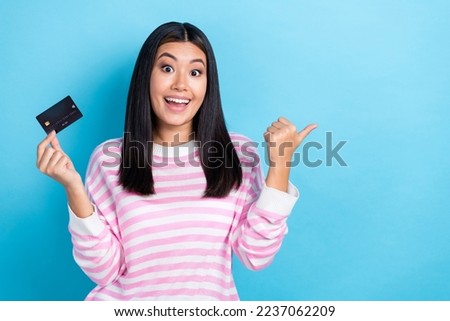 Photo of adorable excited girl dressed pink pullover pointing thumb empty space holding credit card isolated blue color background