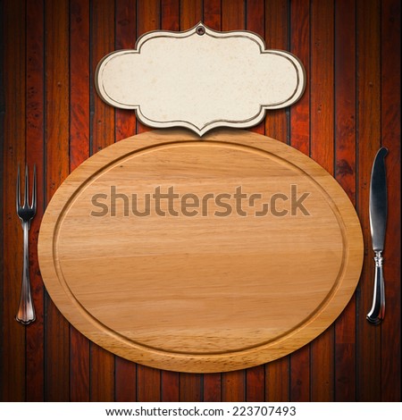 Cutting Board with Cutlery and Label / Wooden oval cutting board with empty label and silver cutlery, fork and knife on wooden table 