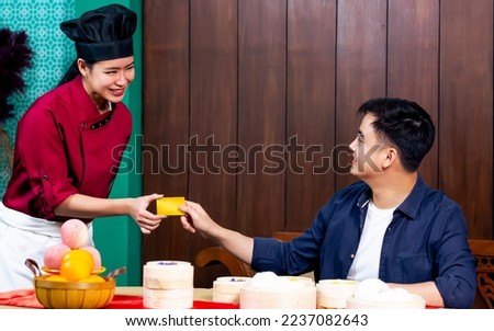 Beautiful professional chef wearing traditional uniform smiling to customer, making payment by credit card, standing in restaurant at hotel. Service mind Concept
