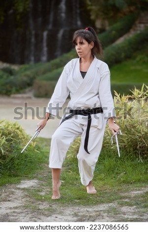 Young karate woman in fighting stance holding a pair of sai outdoors. High quality photo