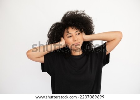 Dreaming young woman looking away covering her ears with hands. Caucasian female model with afro hairstyle and brown eyes in black T-shirt closing her ears concentrating. Silence, privacy concept